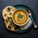 A bright, cozy bowl of coconut curried lentil soup garnished with fresh cilantro and lime wedges, with steam rising to show warmth